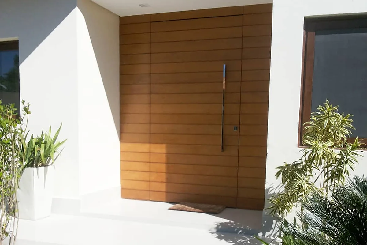Entrada com porta pivotante em madeira e paisagismo
