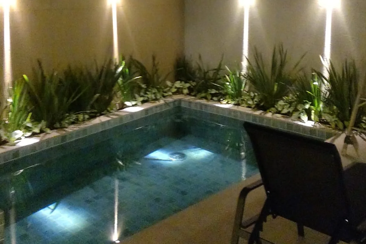 Piscina iluminada à noite, com canteiro e área de descanso